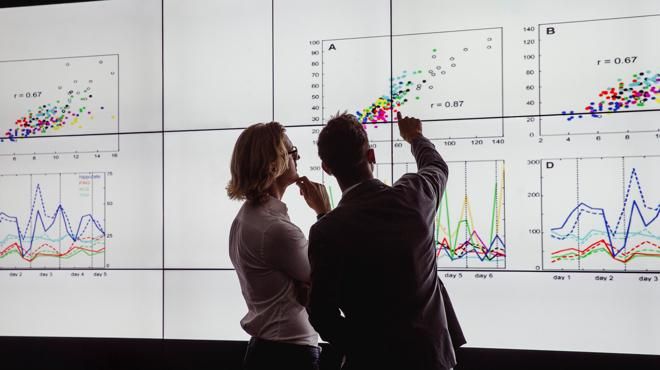 Two people looking at charts on a very large screen