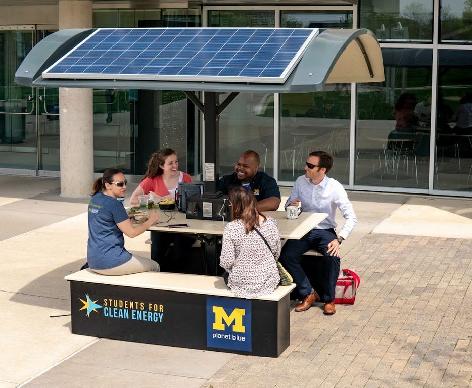 Students sitting an outdoor solar charging booth on campus