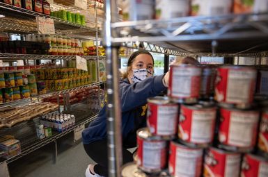 A student wearing a mask stocks shelves in the food pantry