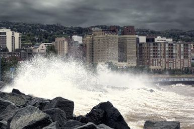 Water crashing onto shore during a storm with a city in the background