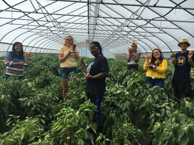 People in a greenhouse holding vegetables