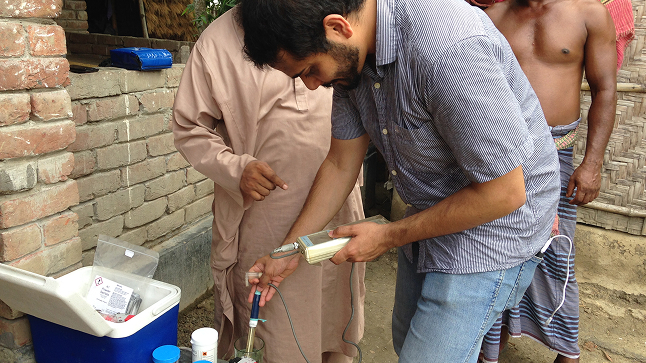A person tests water quality with scientific equipment outdoors, while others observe nearby
