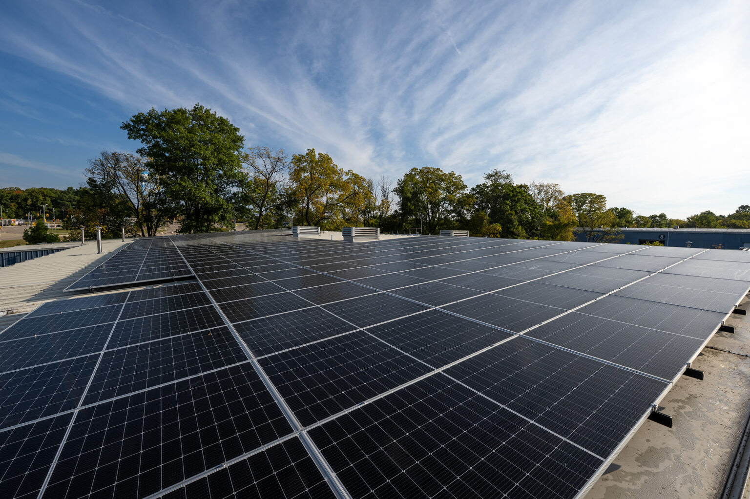 A large array of solar panels on a North Campus build rooftop with trees and a clear sky in the background.